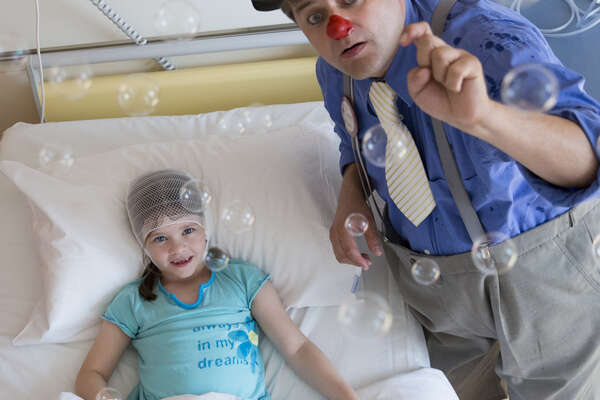 Injured girl in hospital bed smiling about bubbles thrown by a male clown