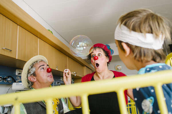 two clowns playing with a bubble in front of hospitalized boy