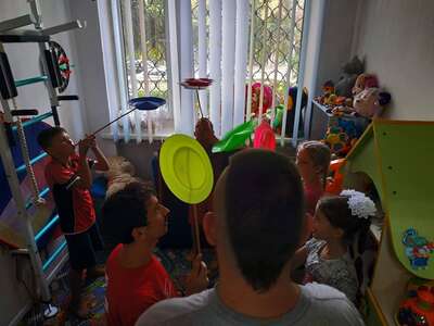Children are practising circus show tricks (spinning plates) in a colourful room.