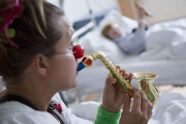 Female clown playing the saxophone to boy in hospital room