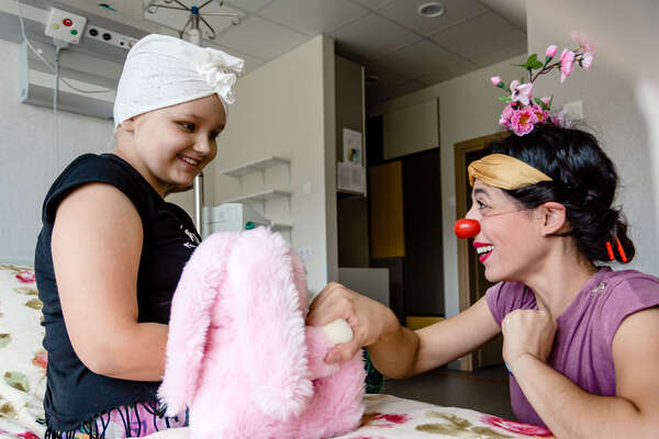 Girl on hospital bed smiling to female clown
